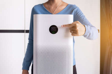 Women hands pointing to screen of white modern air purifier in a living room for refresh air flow at home,Advanced air purifying and protect Pm2.5の写真素材