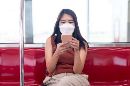 Asian woman wearing face mask and using smart phone on subway trainの写真素材