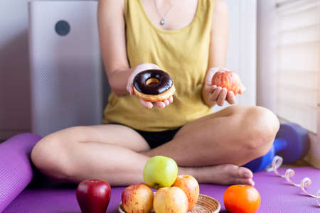 Woman hands holding red apple and baked chocolate donut at home,Healthy diet,Dieting conceptの写真素材