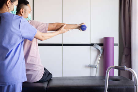 Physiotherapist woman training with man patient using dumbbells in clinic,Physical therapy conceptの写真素材