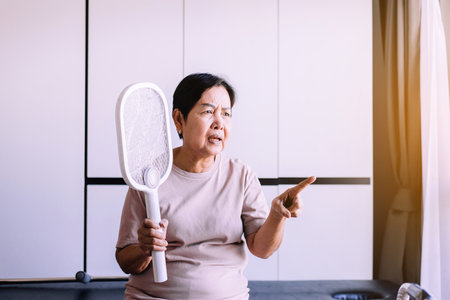 Senior asian woman using mosquito swatter at home,Elderly women with mosquito electric net racketの写真素材
