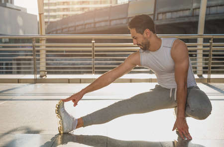 Young man runner stretching for warming up before running or working out