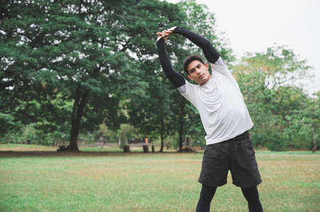 Young man runner stretching for warming up before running or working out in park.の写真素材