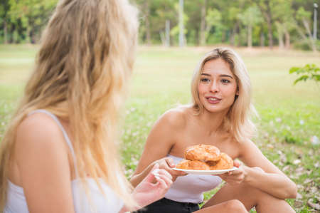 Beautiful woman with friend eatting Croissant while picnic relax in the garden.の写真素材