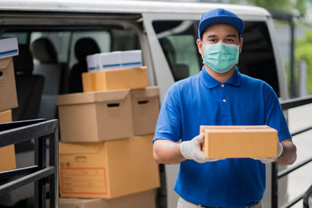 Corona Virus concept, Blue Delivery handsome asian man holding parcel cardboard box and thumbs up...