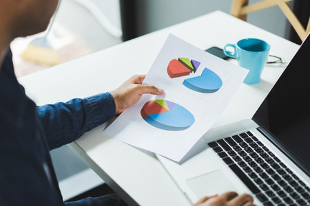 Close up hands businessman using on laptop and holding paper work of financial graph chart data for...