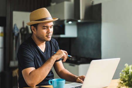 Social distancing concept. Asian handsome man work from home with laptop while showing thumbs up. Young Casual businessman aged around 30 using laptop for his work.の写真素材