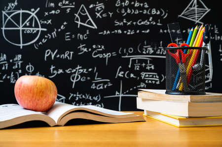 Apple on the opening book. Stationery on the stacking of book in front of blackboard with many...