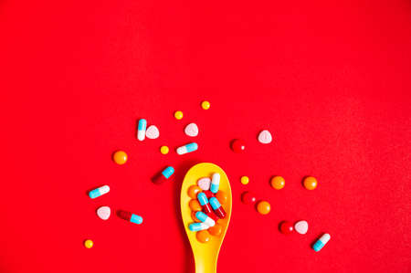 A lot of pills colorful in yellow plastic spoon on the red background. Medicine pills, tablets and capsules with copy space for text.の写真素材