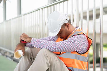 Tired depressed asian civil engineer man sleeping at working construction concrete road site holding...