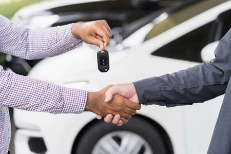 Young man buy the new car. Businessman giving a car key. Salesman car dealing success with customer.の写真素材