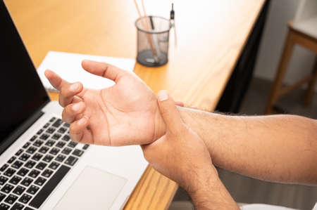 Asian man work so hard and long time that he has office syndrome. He has wrist pain, from working with laptop.の写真素材