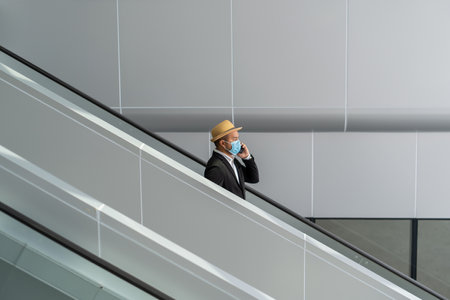 Casual businessman holding trolley bag walking at escalator in the airport terminal. Young man arrive to airport. Safety travel concept.の写真素材