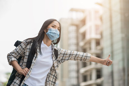 Young beautiful asian woman backpacker traveling in urban city and Hitchhike wearing face mask for protect virus safety travel.の写真素材