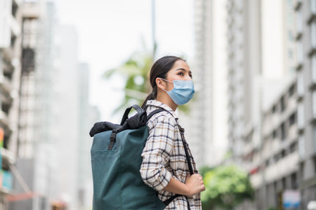 New normal of traveler. Side view of Alone young asian beautiful woman travel in holiday with backpack and wearing protection mask virus for safety trip. She walking alone in the city.の写真素材