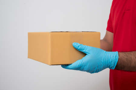 Close up red delivery man wearing rubber glove holding parcel box cardboard sending to customer be...