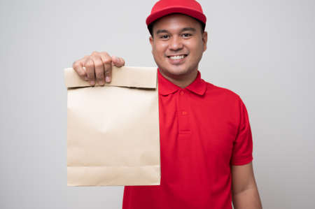 Young asian delivery man in red uniform wearing protection mask and medical rubber gloves using...