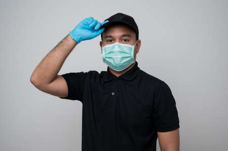 Young asian delivery man in red uniform wearing protection mask and medical rubber gloves using...