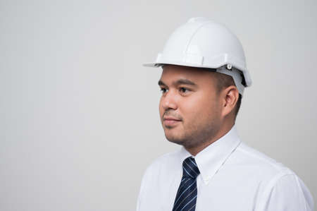 Smiling young asian civil engineer wearing helmet hard hat standing on isolated white background. Mechanic service concept.の写真素材