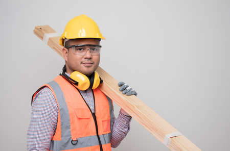 Young asian craftsman carrying wood standing in studio white background. Carpenter in uniform go to working.の写真素材