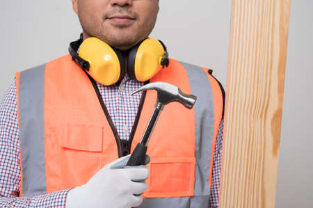 Close up craftsman holding wood and hammer standing in studio white background. Carpenter in safety...