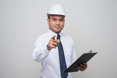 Asian manager civil engineer in uniform hard hat holding clipboard working in studio isolated white background.の写真素材