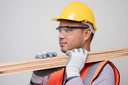 Young asian craftsman carrying wood standing in studio white background. Carpenter in uniform go to...