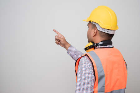 Rear view asian civil engineer standing and pointing finger to blank space. Worker wearing hard hat on isolated white background.の写真素材