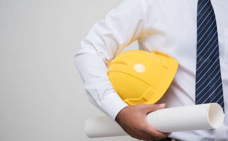Close up civil engineer holding helmet hard hat and paperwork blueprint roll standing post in studio on isolated white background. Architecture or engineer concept.の写真素材
