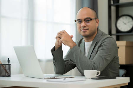 A man around the age of 35. Working at home by meeting video conference looking at camera. He was wearing a grey suit and glasses. Asian businessman work from home talking on screen.の写真素材