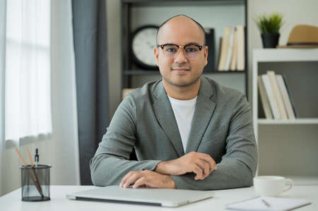A man around the age of 35. Working at home by meeting video conference looking at camera. He was wearing a grey suit and glasses. Asian businessman work from home talking on screen.の写真素材