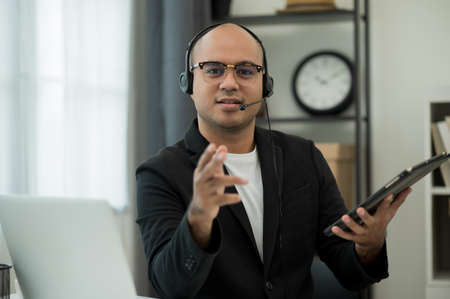 A middle-aged man around the age of 35. Working at home  conference talking on phone and showing thumbs up. He was wearing a grey suit and glasses. Smiling asian businessman work from home.の写真素材