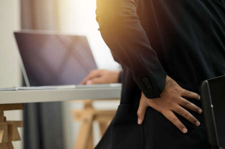Salaryman working his laptop computer suddenly he feeling pain in back and waist He try to relax and relieve by his hand.の写真素材