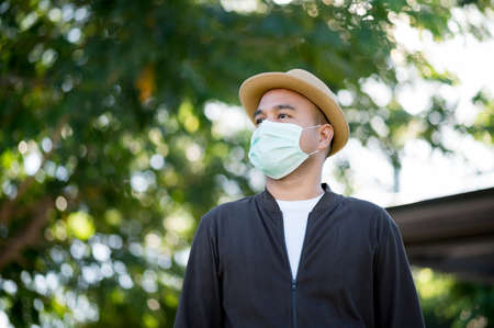 Asian freelancer put on brown hat and face mask working outdoor. Office worker or businessman stand...