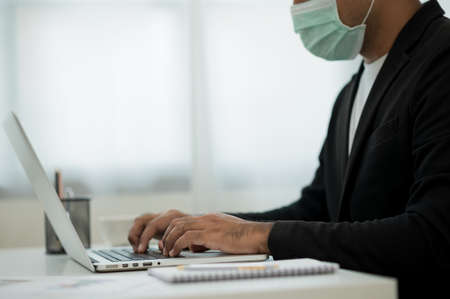 Young businessman wearing protection mask working with laptop in office. Social distancing safety from  virus flu.の写真素材