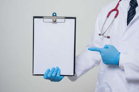 Close up Asian bald Doctor in white coat, stethoscope, blue glove wearing face mask pointing finger to paper on clipboard isolated on white background.の写真素材