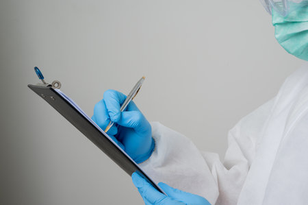 Close up A portrait of virologist put on PPE suit writing clipboard with pen isolated on white background. Personal Protective Equipment Concept.の写真素材