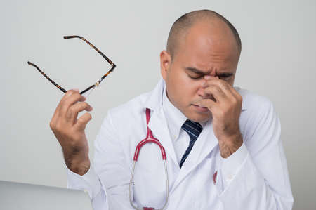 A portrait of Asian doctor put on stethoscope hand on head for pain in head because stress sitting at the desk isolated on white background.の写真素材