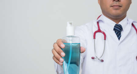 Close Up Asian bald Doctor in white coat, stethoscope, blue glove showing alcohol hand gel and get thumb up isolated on white background.の写真素材