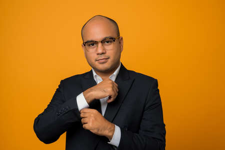 Business bald man wearing glasses standing look at camera touching sleeve of suit isolated on yellow...