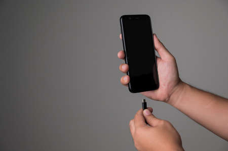 Low battery of smartphone. Male hands holding smartphone and charging with cable line. Cell phone...