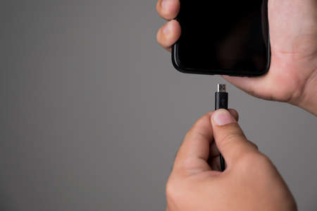 Low battery of smartphone. Male hands holding smartphone and charging with cable line. Cell phone...