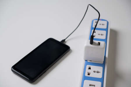 The power bank is charged on a power strip on the white table. Electrical equipment, electrical wires and power strips in the house.の写真素材