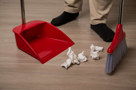 Close up young man sweeping the red broom holding dustpan to cleaning paper garbage on floor in the...