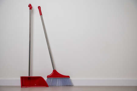 Close up red broom and dustpan on floor in the house. Home cleaning equipment red color.