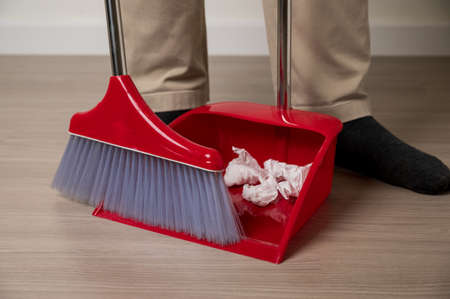 Close up young man sweeping the red broom holding dustpan to cleaning paper garbage on floor in the...