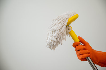 Close up male hand wearing rubber glove holding the mop ready to cleaning the living room in his house. Home cleaning service concept.の写真素材