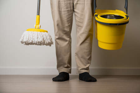 Man standing holding the yellow mop and bucket in cleaning the living room in his house. Home...