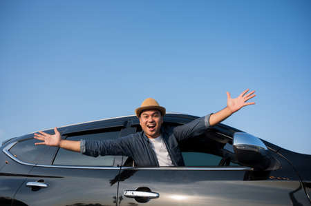 A young Asian man drives a car on a clear day. With beautiful blue sky. He driving to travel by car.の写真素材