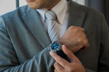 A handsome, well-dressed business man is standing looking at the watch.の写真素材